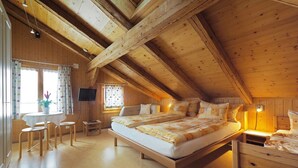 Un dormitorio acogedor en el ático, con una cama grande, vigas de madera, un escritorio y un televisor.