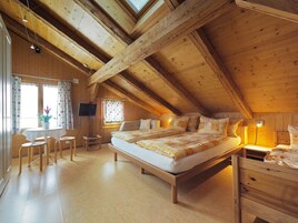 Un dormitorio acogedor en el ático, con una cama grande, vigas de madera, un escritorio y un televisor.