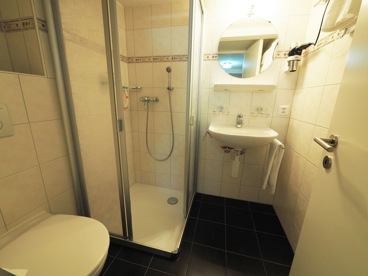 Un baño pequeño y moderno con cabina de ducha de vidrio, un lavamanos blanco y un inodoro.