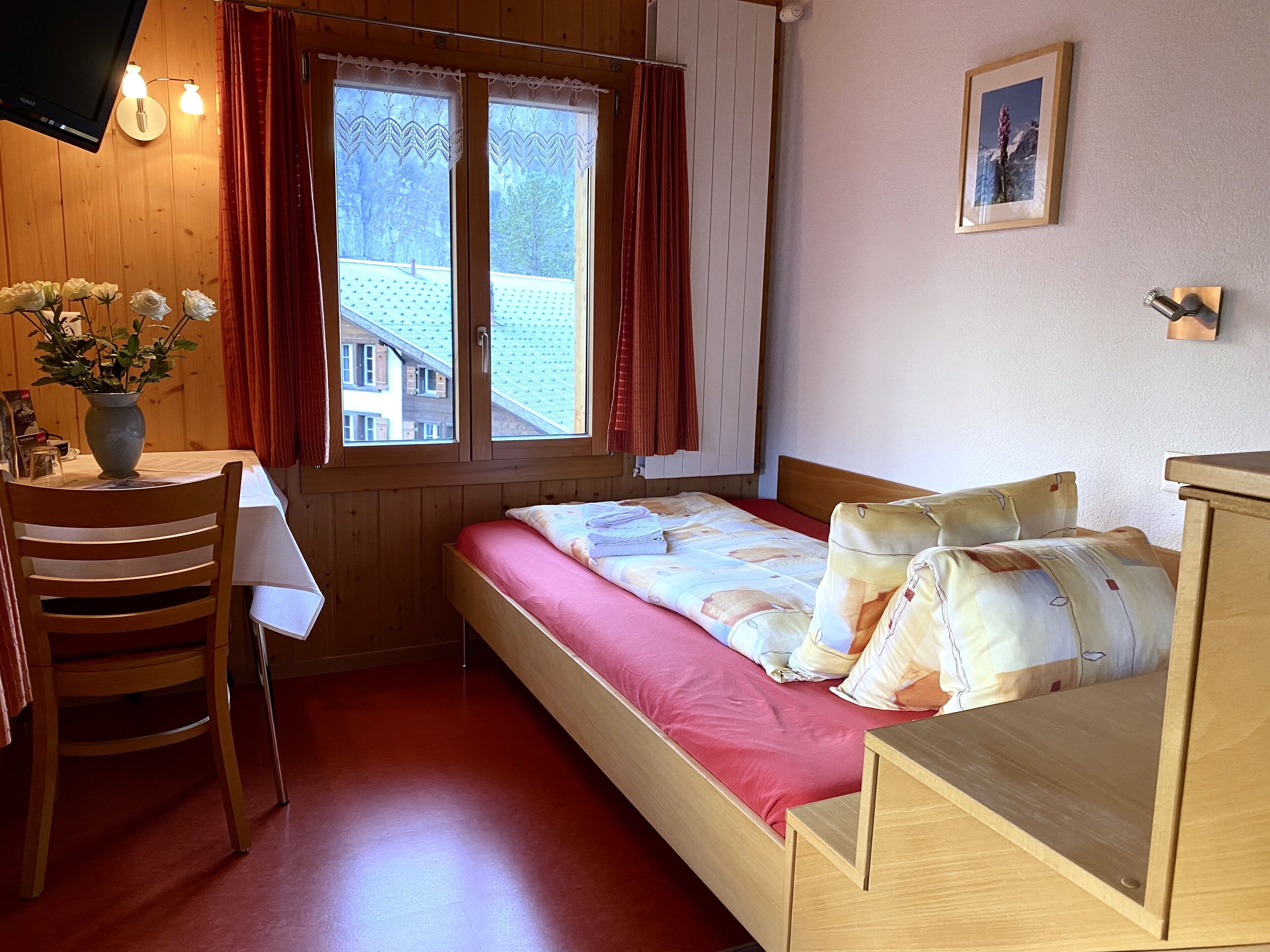 A small, cozy room with a bed, a desk, and a window with curtains.