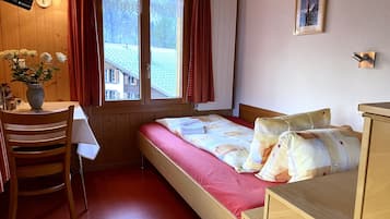 A small, cozy room with a bed, a desk, and a window with curtains.