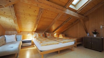 A cozy attic bedroom with a wooden sloped ceiling, a large bed, a sofa, and a cabinet.