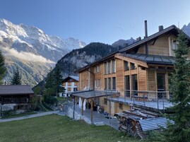 A wooden chalet with a balcony, set against a mountainous backdrop.