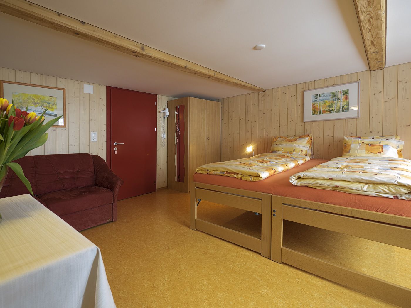 A room with a bed, a red door, a wooden ceiling, and a painting on the wall.
