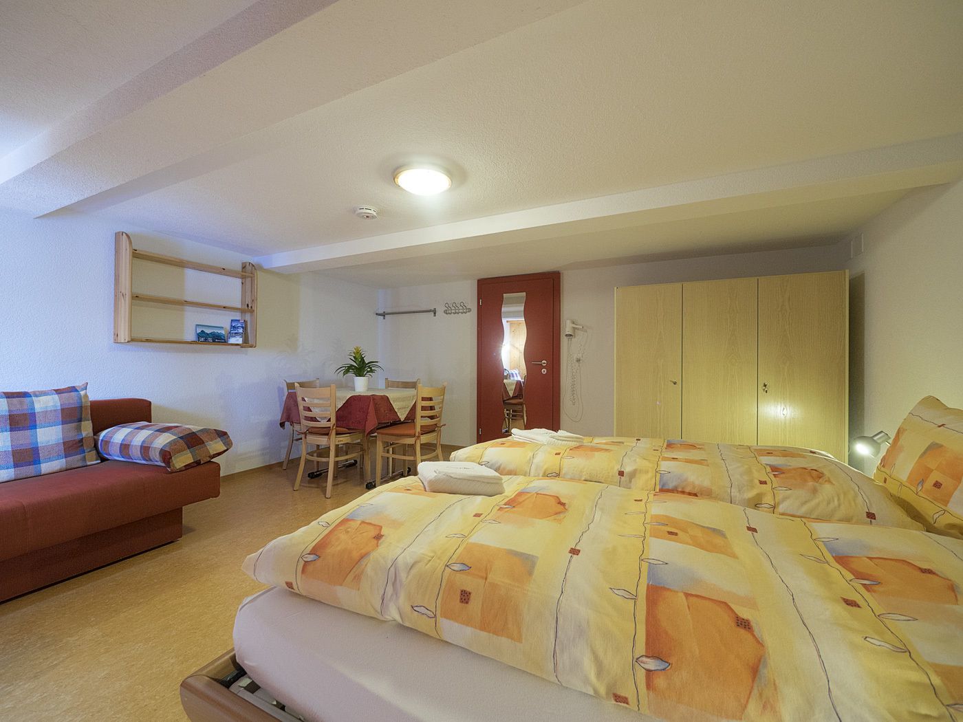 A bedroom with a bed, a sofa, a dining table with chairs, a wardrobe, and a bathroom visible through an open door.