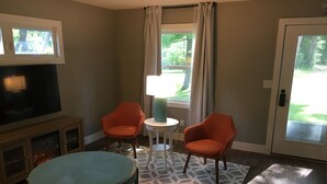 A living room with a television, two orange chairs, a round table, a lamp, and a patterned rug. - Village of Elk Rapids Walk to Beach (Elk Rapids)