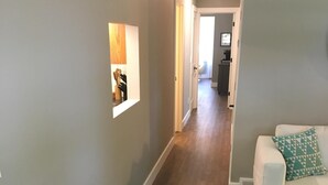 A hallway with a wooden floor, a white couch with a patterned pillow, and a geometric rug. - Village of Elk Rapids Walk to Beach (Elk Rapids)