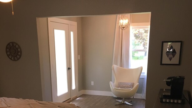 A bedroom with a bed, a chair, a coffee machine, and a door leading to a balcony. - Village of Elk Rapids Walk to Beach (Elk Rapids)
