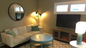 A living room with a sofa, a coffee table, a TV, and a fireplace. - Village of Elk Rapids Walk to Beach (Elk Rapids)