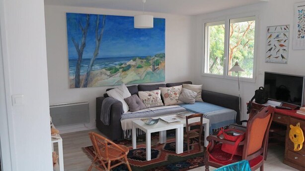 A living room with a large painting of a beach scene, a sofa with cushions, a small table, a TV, and a chair. - 004 - Relaxation and rest in this house 2 steps from the ocean (SOULAC SUR MER)