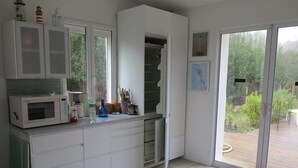 A modern kitchen with white cabinetry, a microwave, and a window overlooking a garden. - 004 - Relaxation and rest in this house 2 steps from the ocean (SOULAC SUR MER)