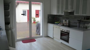 A modern kitchen with white cabinets, a built-in oven, and a large sliding glass door leading to an outdoor patio area. - 004 - Relaxation and rest in this house 2 steps from the ocean (SOULAC SUR MER)