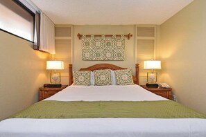Une chambre d’hôtel avec un grand lit, deux lampes de chevet, une tête de lit en bois, une décoration murale et une fenêtre avec des stores.