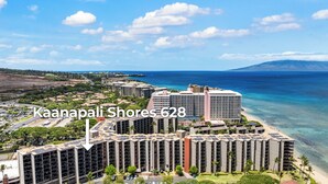 A high-rise hotel with multiple floors, located near a beach with clear blue waters and a mountainous backdrop.