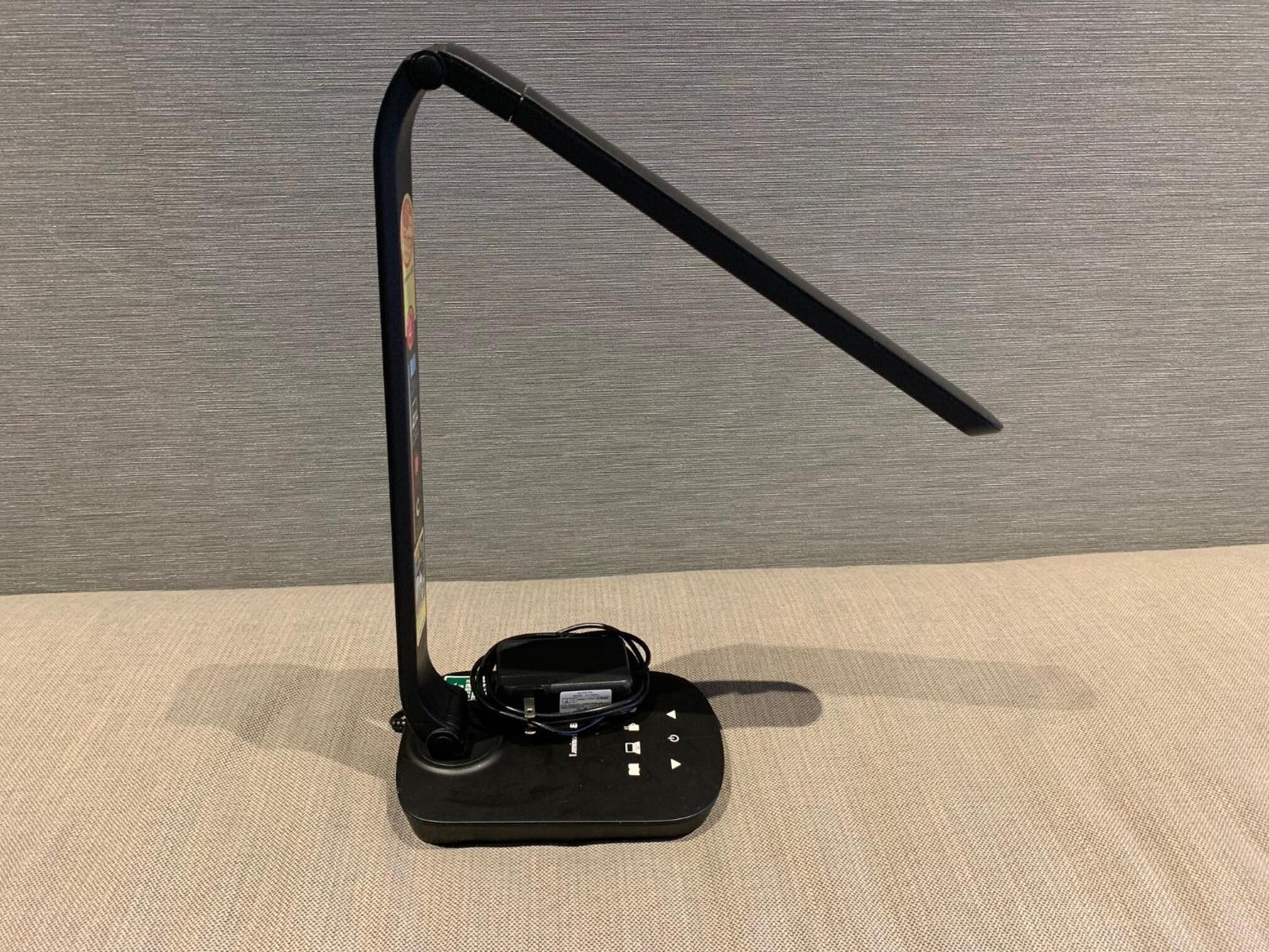 A black electronic device with a curved stand and a cable, placed on a textured surface.