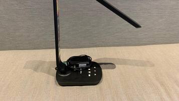 A black electronic device with a curved stand and a cable, placed on a textured surface.
