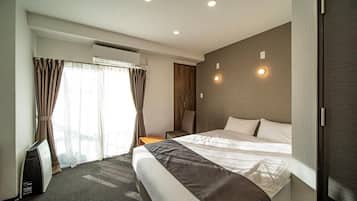 A hotel room with a bed, a bedside table, a lamp, and a window with curtains.