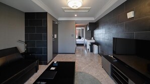 Un hall d’hôtel moderne avec un canapé en cuir noir, une table basse noire et un téléviseur à écran plat posé sur un meuble en bois foncé.