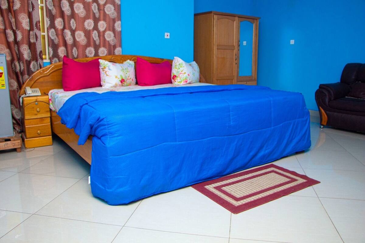A bedroom with a bed, a wooden wardrobe, a blue wall, and a patterned curtain.