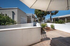 A covered outdoor area with a wooden deck, white walls, and a large umbrella providing shade.