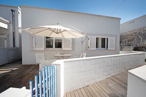 Un patio exterior moderno con un muro blanco, una terraza de madera y un paraguas blanco.
