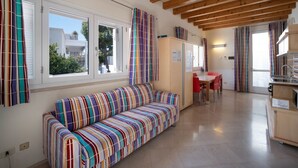A modern interior with a striped sofa, wooden beams, a dining area, and a kitchen. - WePuglia - Residence Cala Paura - Apt. Vecchio Frack (Polignano A Mare)