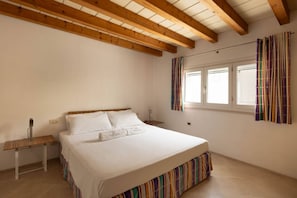 A bedroom with a bed, a bedside table, a window with curtains, and wooden beams on the ceiling.