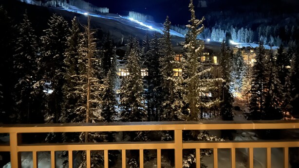 A snow-covered landscape with a building illuminated by lights, surrounded by trees.
