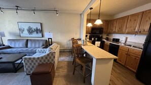 A compact living space with a sofa, ottoman, and chairs, a kitchenette with wooden cabinets, and a dining area with a table and chairs.