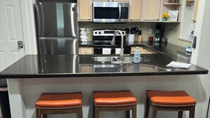 Une cuisine dotée d’un grand îlot central, d’appareils électroménagers en acier inoxydable, de meubles de rangement en bois et d’un luminaire suspendu.