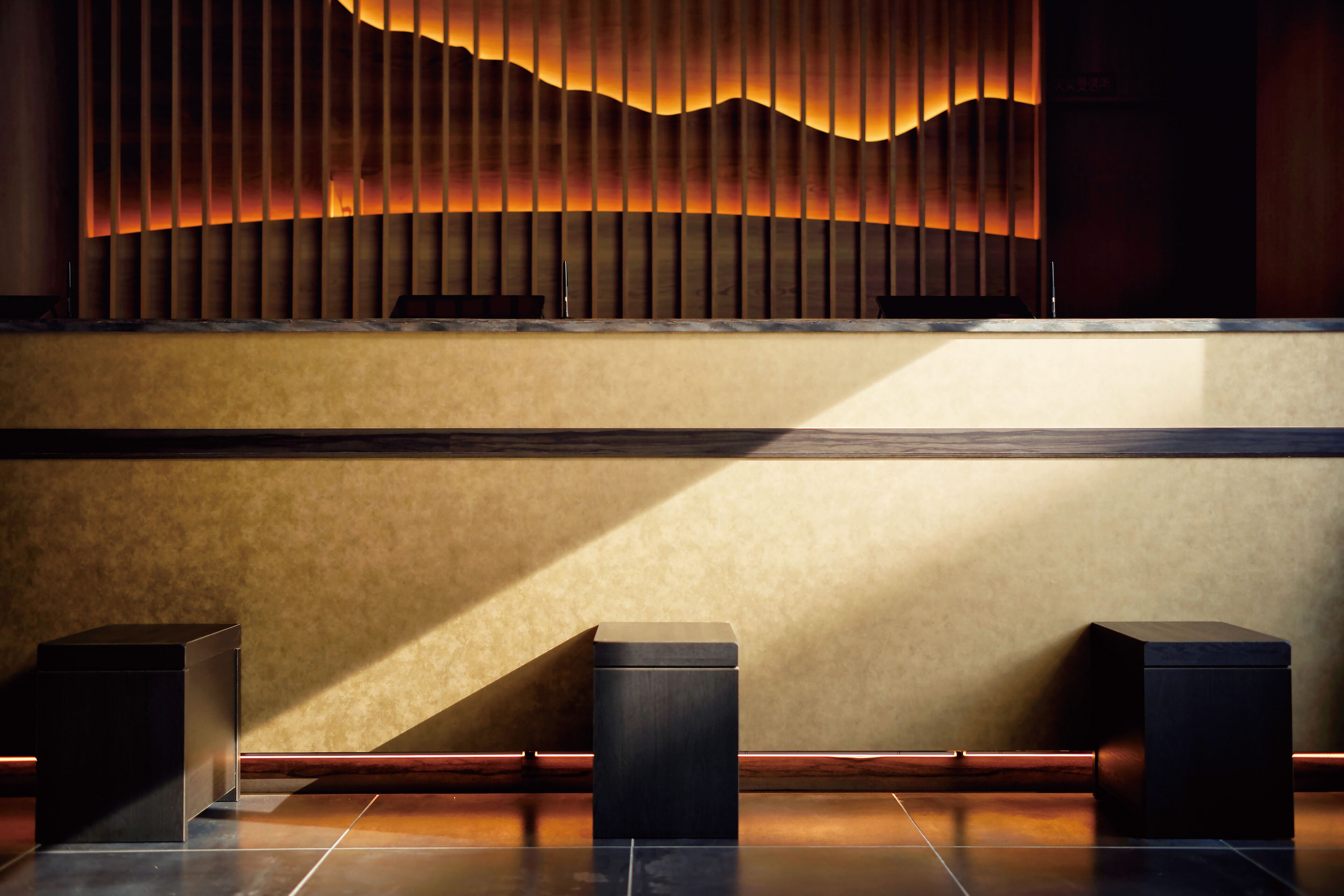 A reception area with a modern design, featuring a wooden panel wall, a reception desk, and two black square stools.