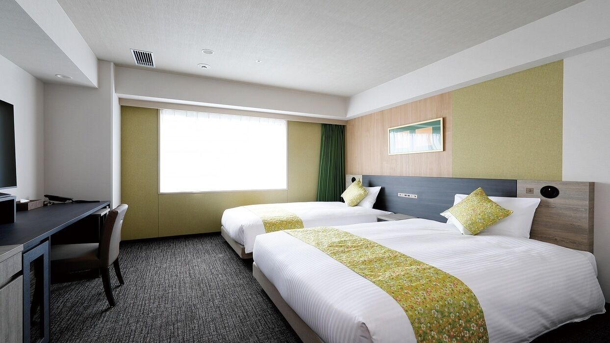 A hotel room with two beds, a desk, a chair, a window, and a painting on the wall.