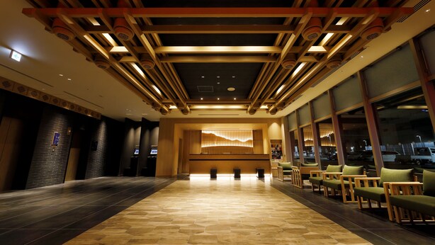 A hotel lobby with a long reception area, a seating area with chairs, and a modern ceiling design. - Daiwa Roynet Hotel Nara Natural Hot Springs (Nara)