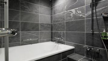 A modern bathroom with a bathtub, shower, and a small vanity area.