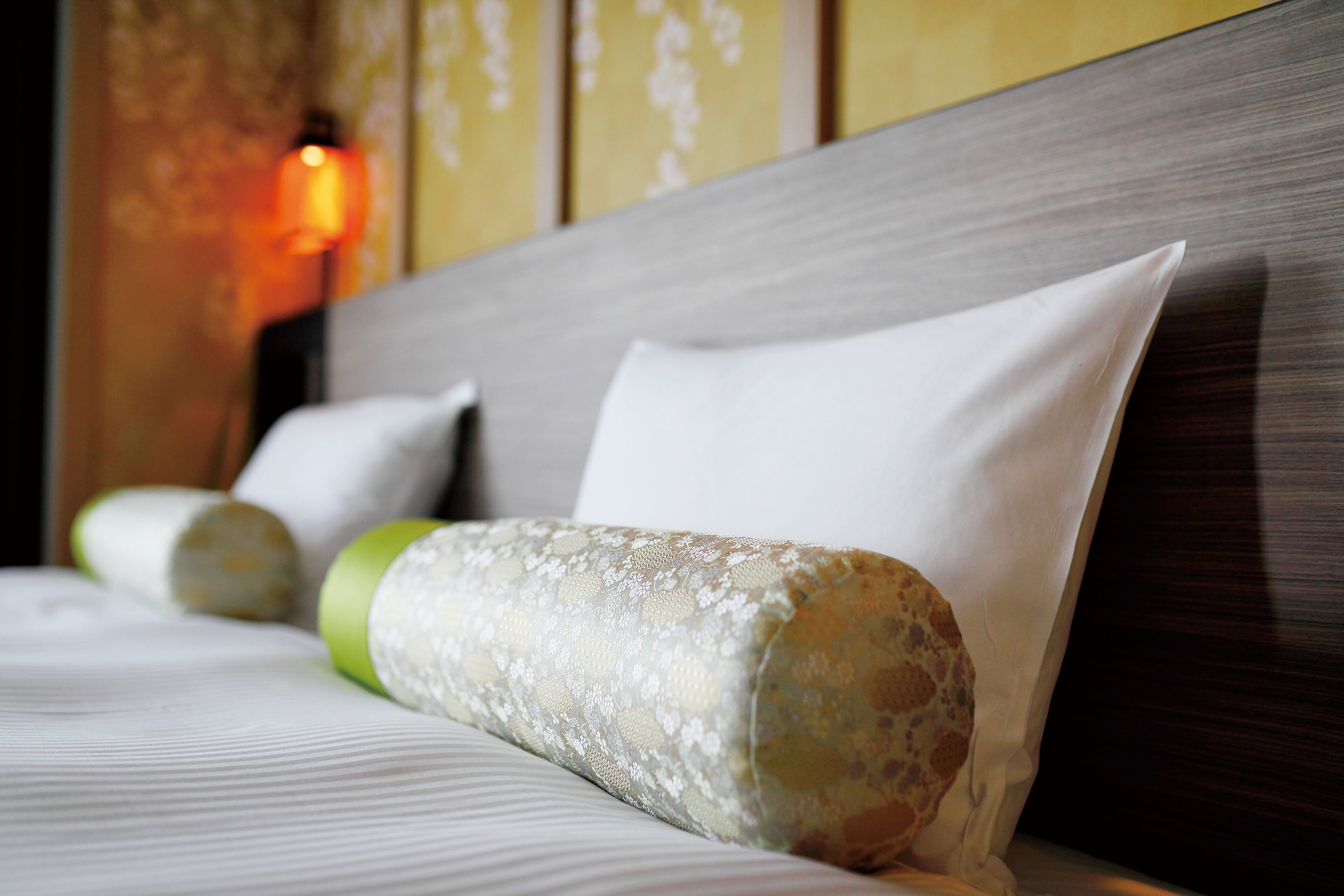 A neatly made bed with a pillow and a rolled-up blanket.