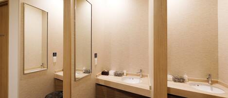 A modern bathroom with two sinks, a mirror, and a trash bin.
