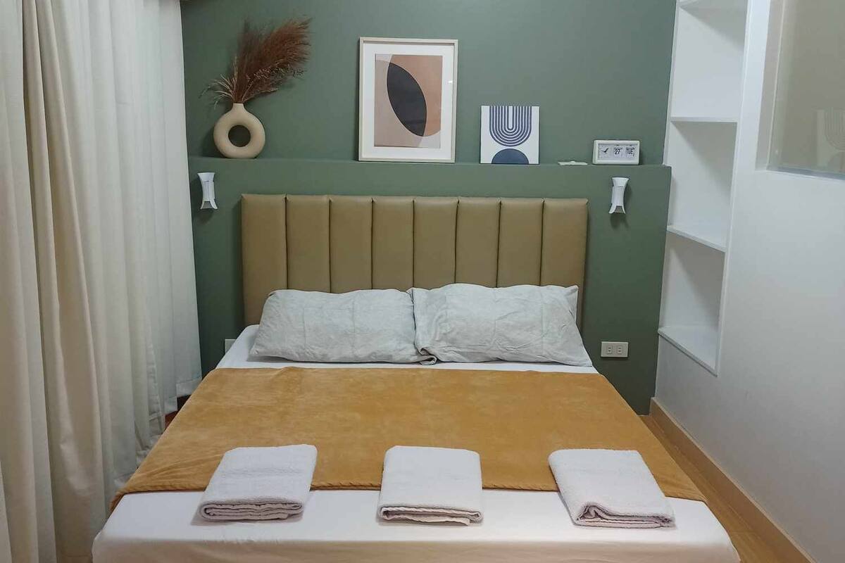 Ein ordentlich bezogenes Bett mit Kopfteil, einem Nachttisch und einem an der Wand befestigten Regal mit Dekoration.