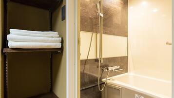 Une salle de bain équipée d’une douche, d’une baignoire et d’une étagère où sont pliées les serviettes.
