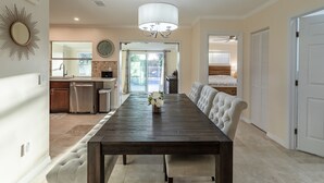 A spacious dining area with a dark wooden table, white upholstered chairs, and a chandelier.