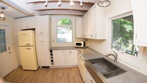 Cocina compacta con armarios blancos, microondas integrado, pileta y ventana con vista a follaje.
