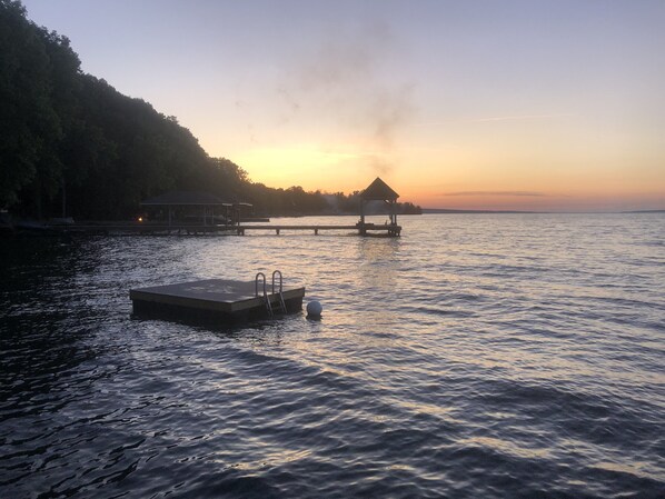A dock with a small platform and a gazebo at the end, surrounded by calm water and a forested hillside. - 120 Feet of Private Beachfront (Trumansburg)