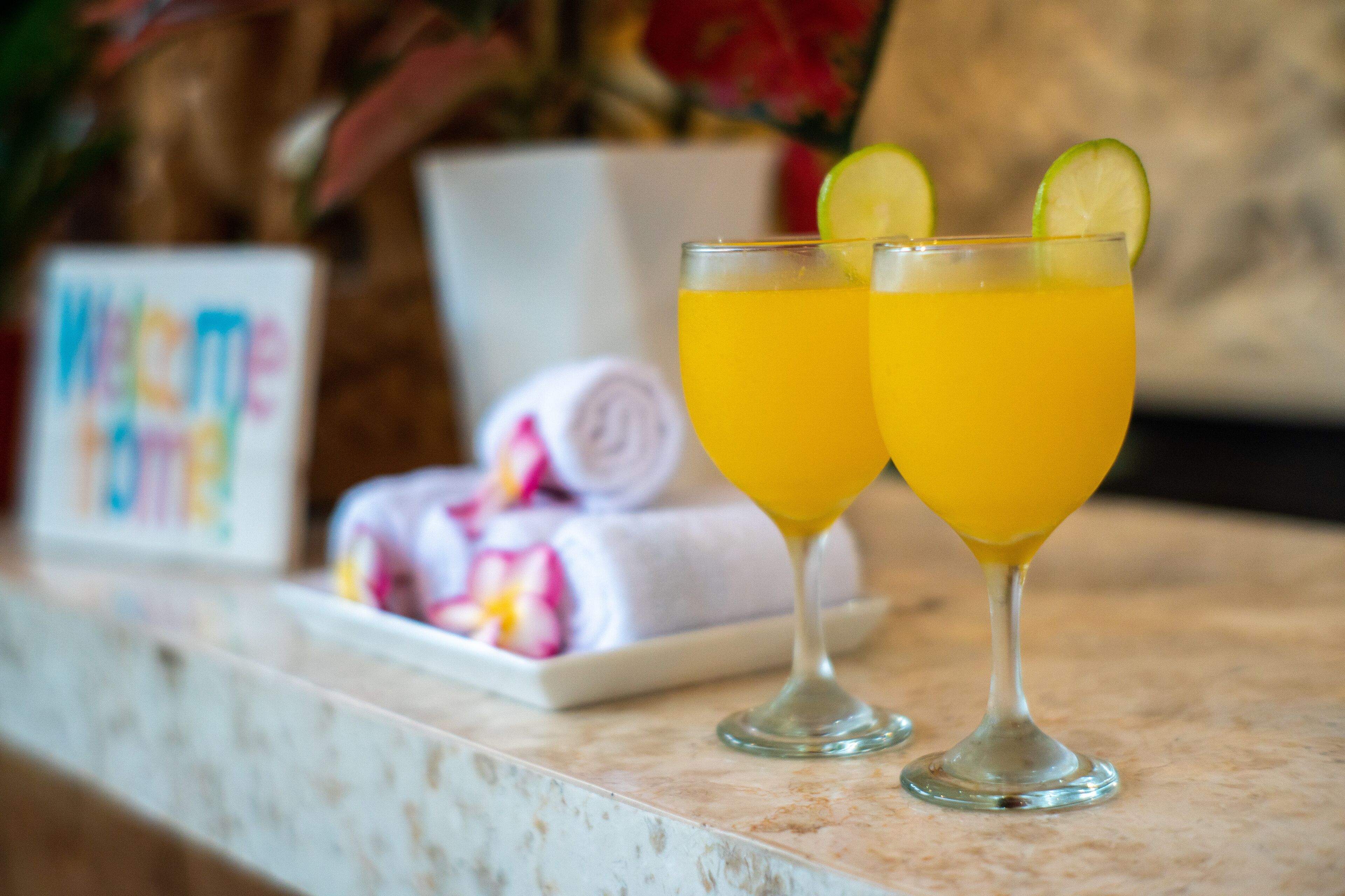 Two glasses of orange juice on a marble countertop with a towel and a sign in the background.