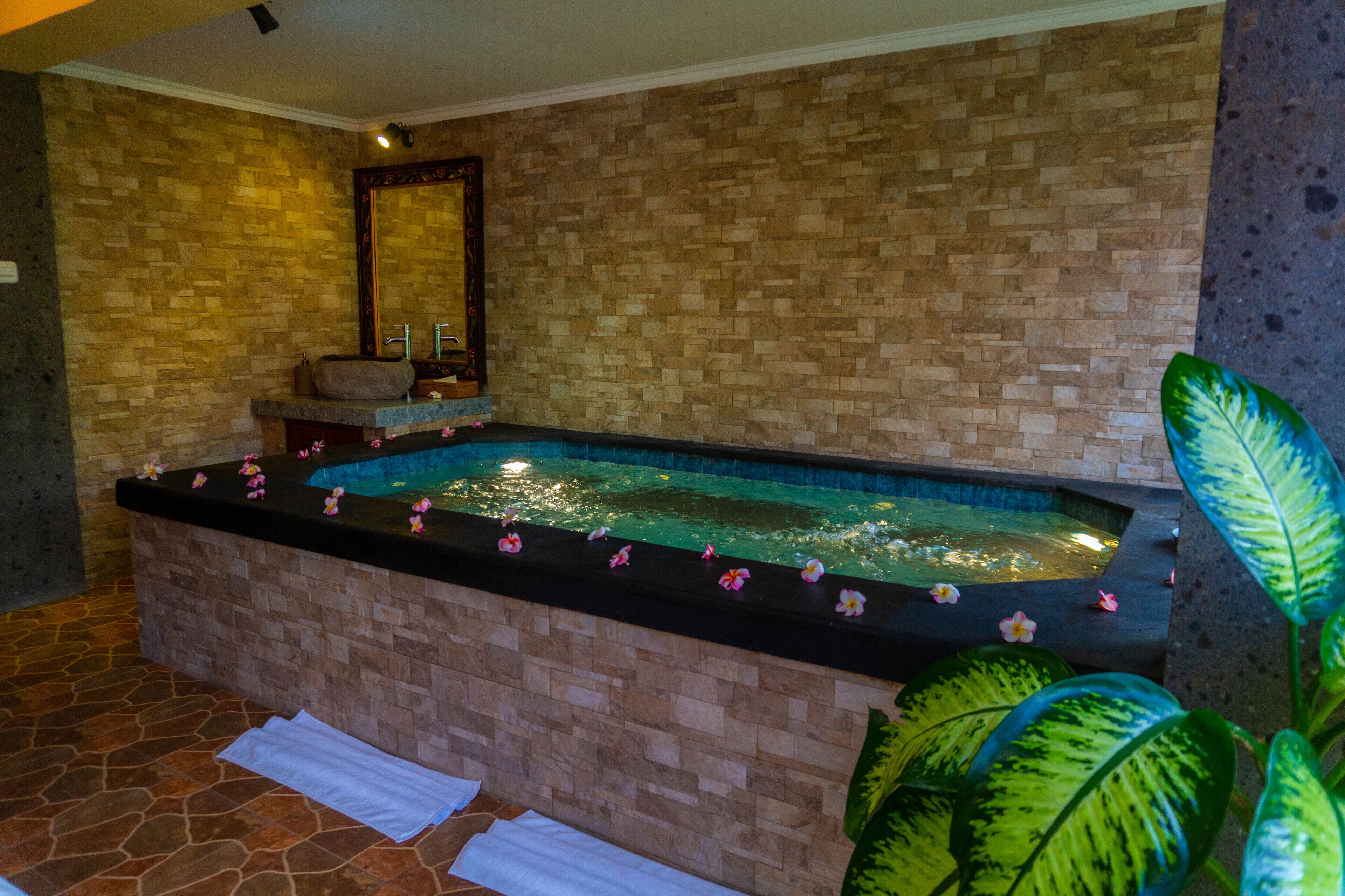 Ein Wellnessbereich mit Steinwand, einer großen Badewanne und einem Spiegel.
