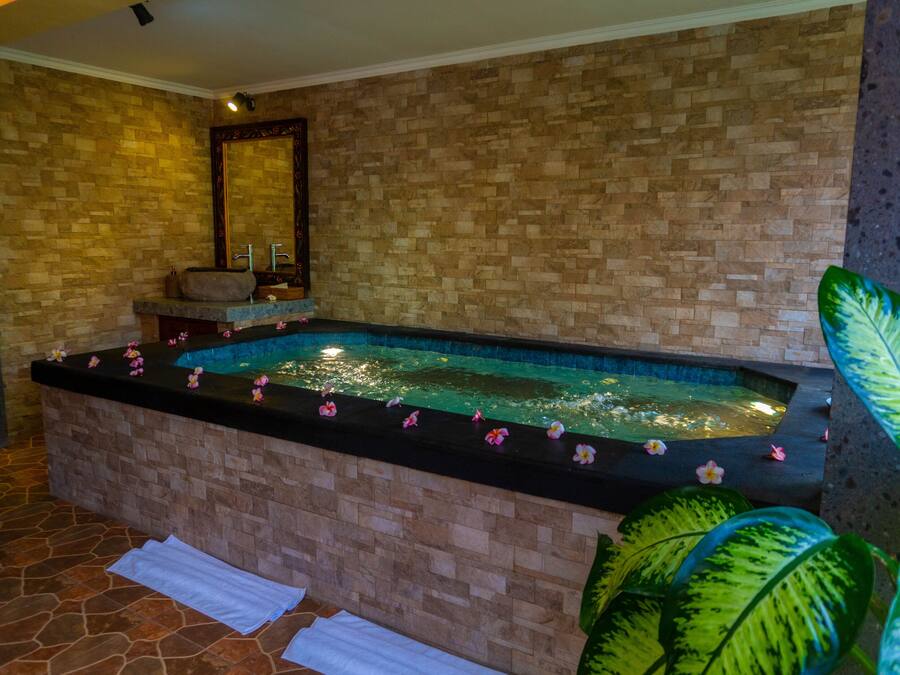 Ein Wellnessbereich mit Steinwand, einer großen Badewanne und einem Spiegel.