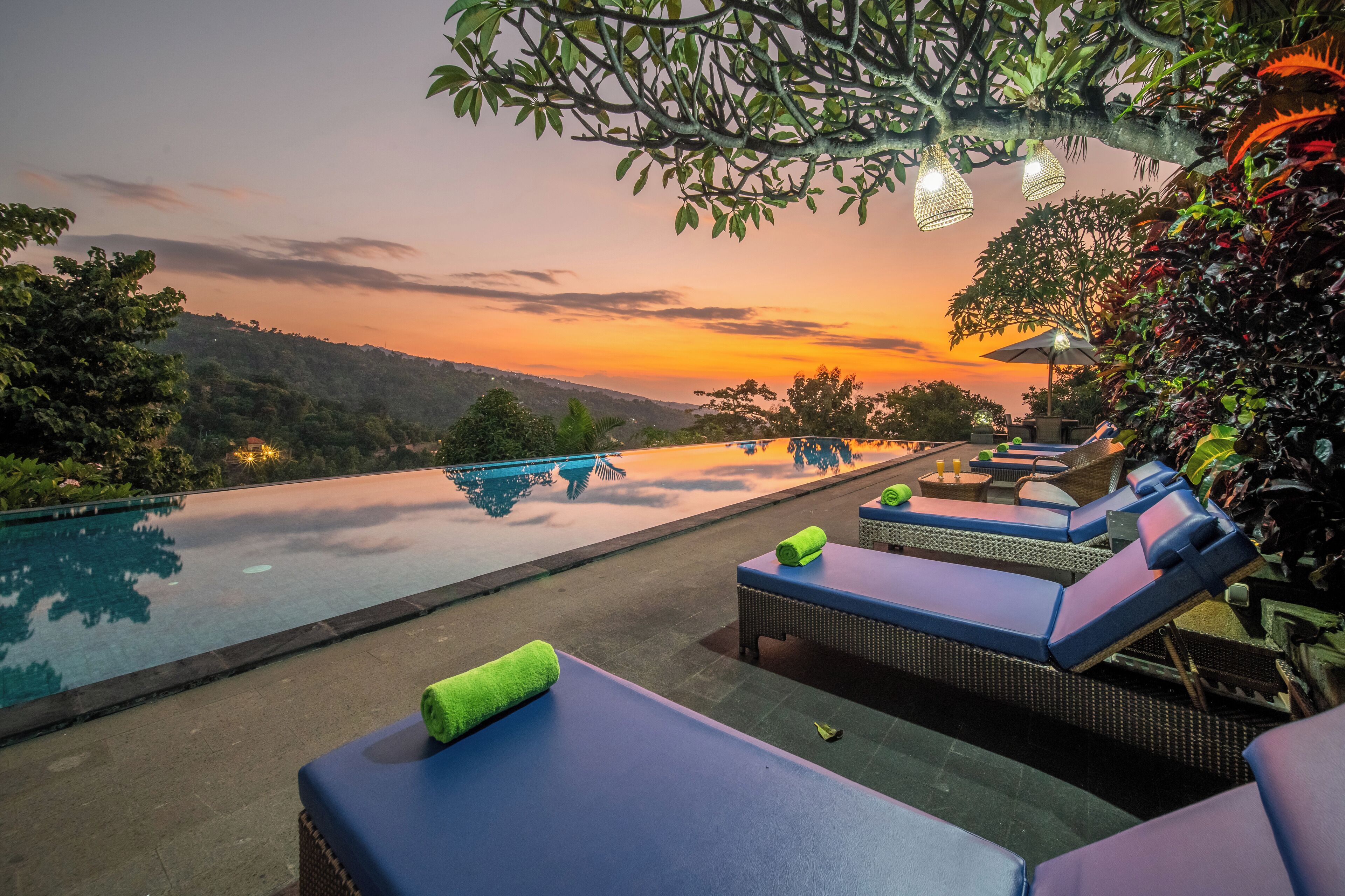 A poolside area with lounge chairs and a view of a sunset over a hilly landscape.