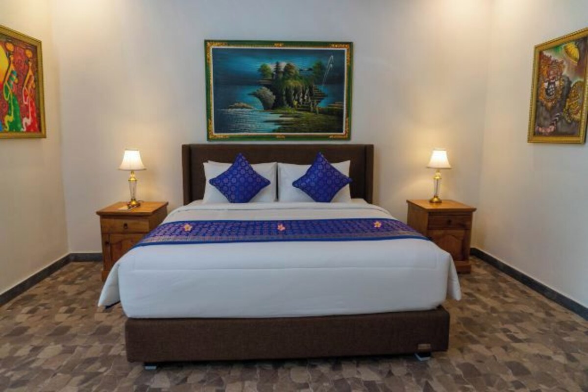 A hotel room with a large bed, two nightstands, and a painting above the bed.