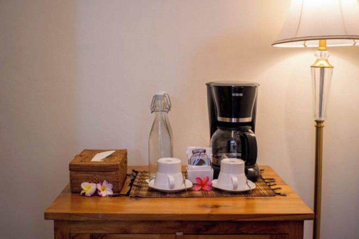 A wooden table with a coffee maker, two cups, a bottle, and a box, all on a placemat.