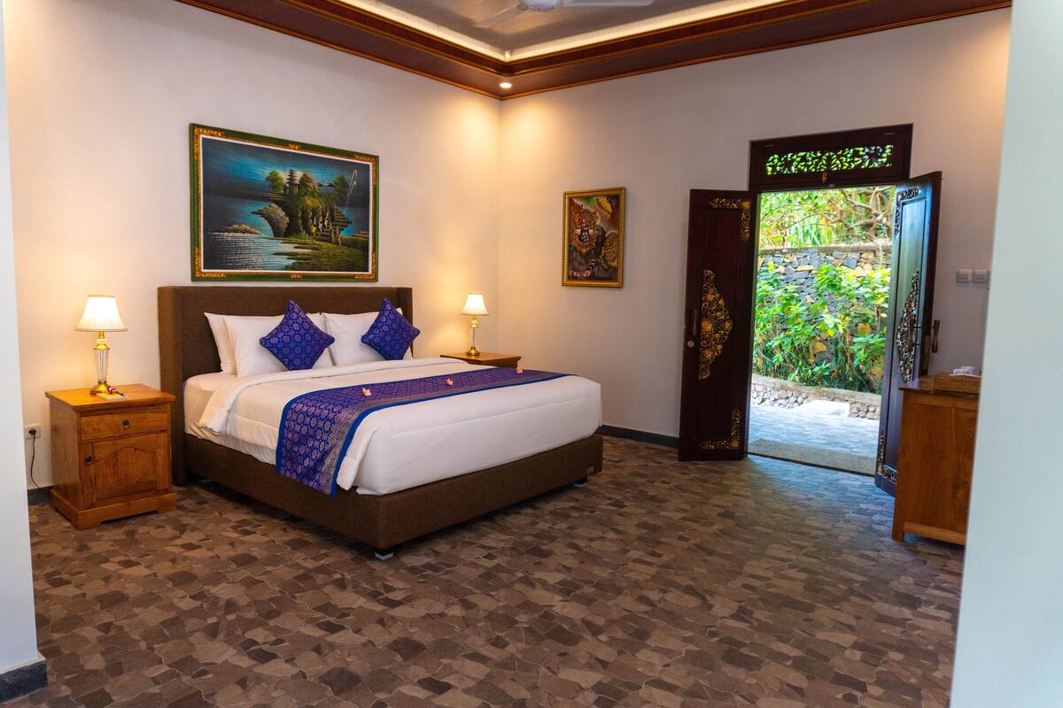 A neatly made bed with a blue and white bedspread, two bedside lamps, and a painting above the bed.