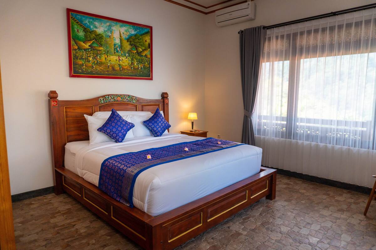 A neatly made bed with a wooden headboard, a nightstand with a lamp, and a painting on the wall.