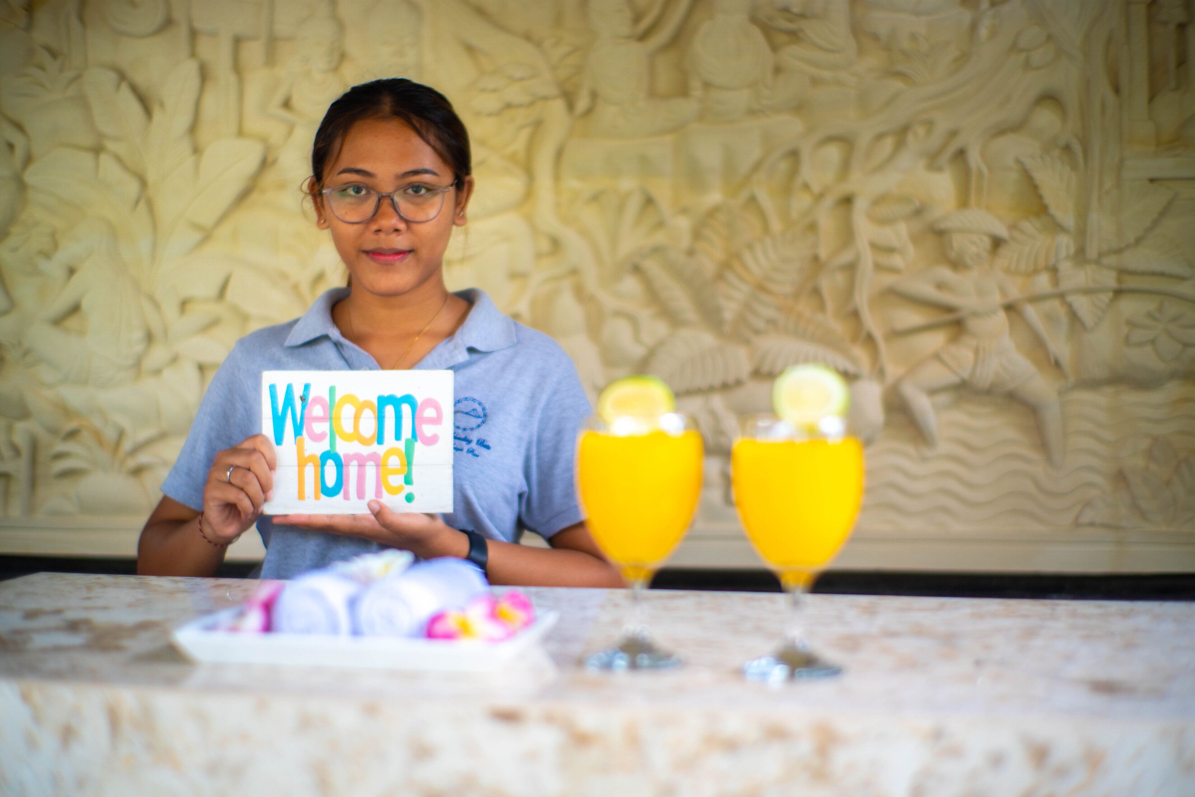 A person holding a 'Welcome home!' sign at a table with a decorative wall in the background.